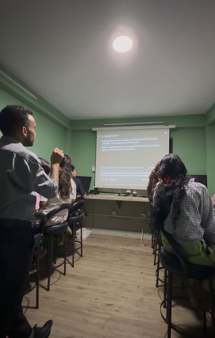Students seated on stools in the school computer room, watching a projected screen while a facilitator stands at the side of the room.