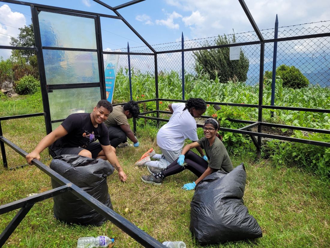 Four volunteers filling rubbish bags at the Chhaimale village project, hillside and cornfield behind them.