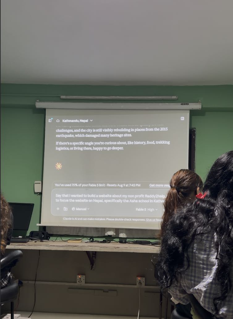 An AI assistant conversation projected on a pull-down screen in the school computer room, showing a question about building a website for the Asha school in Kathmandu.
