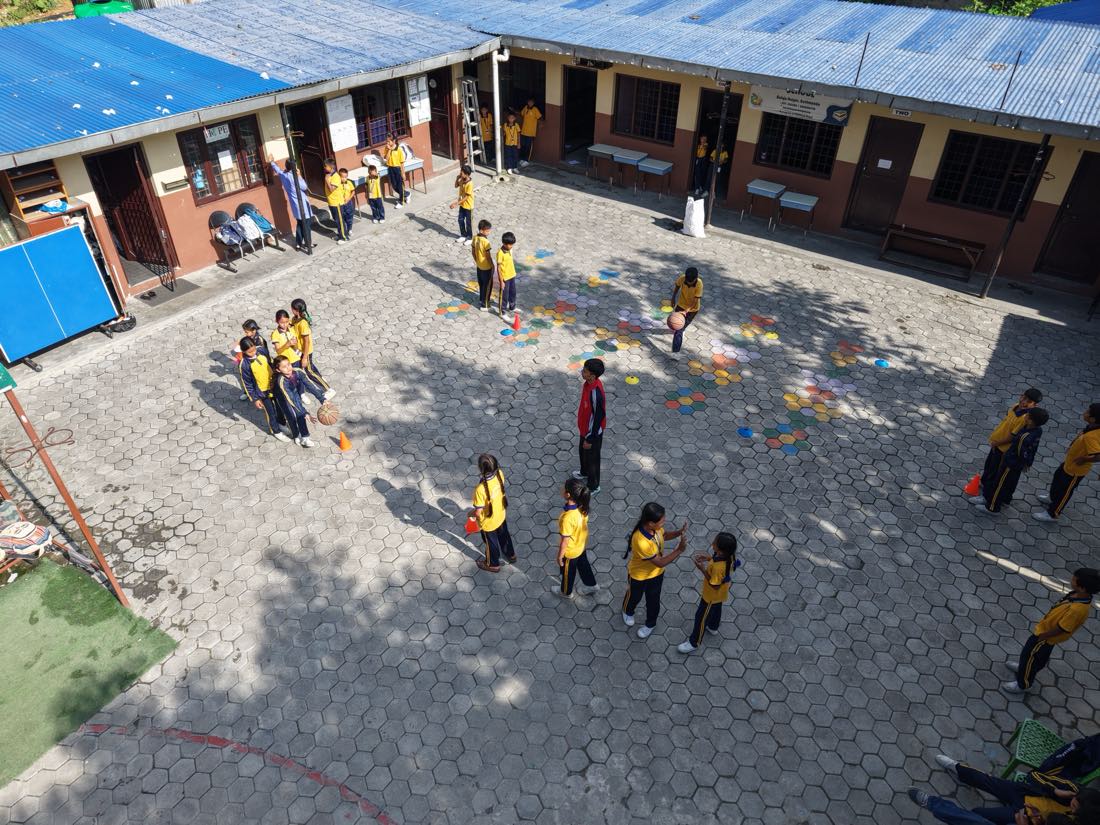 Students playing basketball in the Asha Vidhyashram School yard, classroom doorways lining two sides of the courtyard.