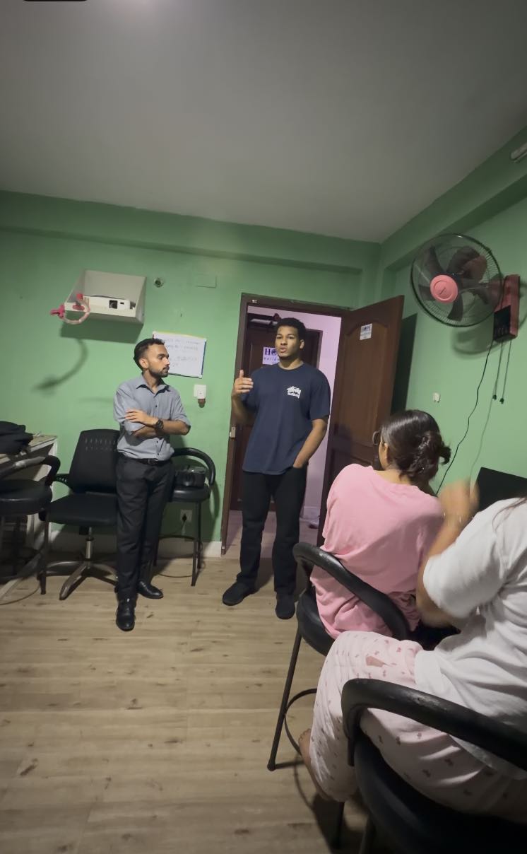 Diwas Rathod and Shawn Reddy standing at the front of the school computer room, talking with two students seated in office chairs.